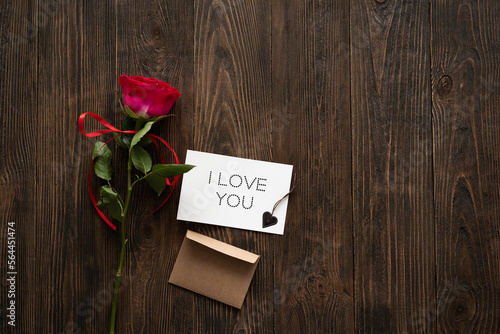 I love you. Red rose with postcard on wooden background. Happy Valentines Day postcard. Love concept for mothers day or valentines day. Valentine card with space for text