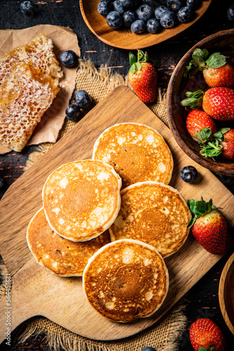 Pancakes on a wooden cutting board with honey and berries.