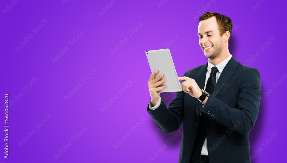 Portrait of smiling businessman in black suit using touchpad tablet pc, on violet purple background. Success in business concept studio picture. Copy space for ad text. Portrait of smiling businessman in black suit using touchpad tablet pc, on violet purple background. Success in business concept studio picture. Copy space for ad text.
