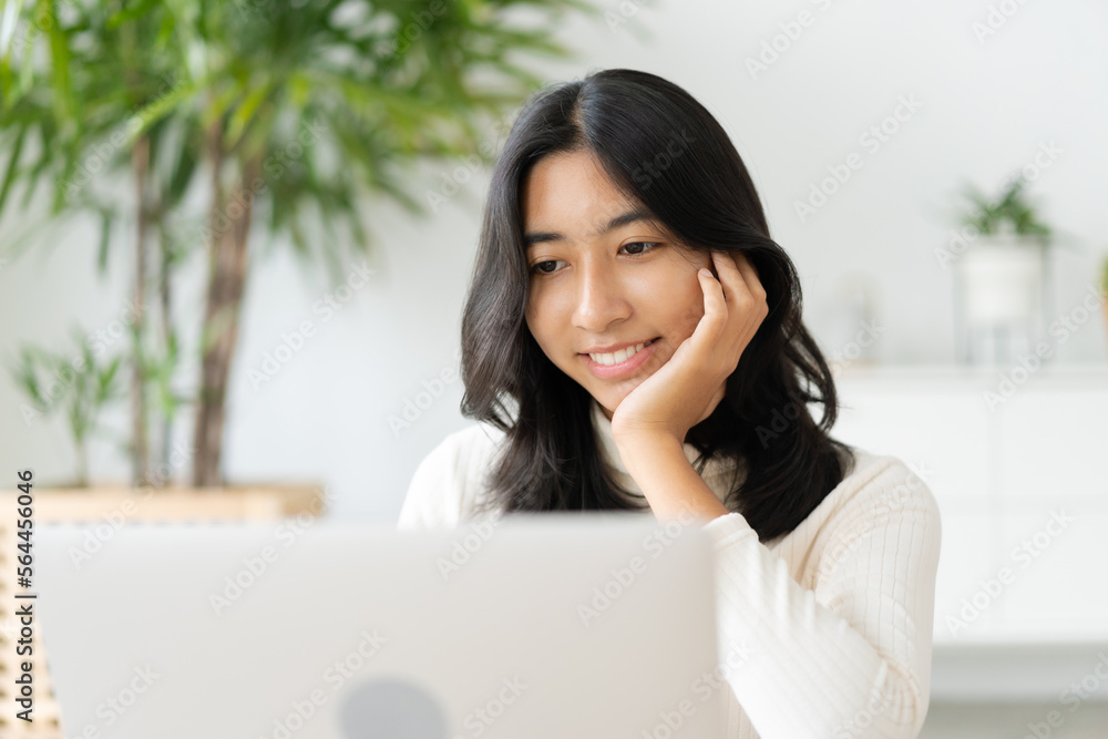 Asian woman touching chin and using laptop at home Asian woman touching chin and using laptop at home