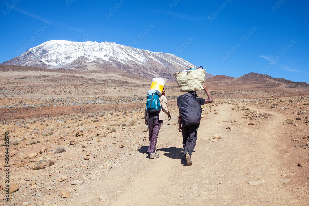 Porters carrying heavy load on his back walks along the road.