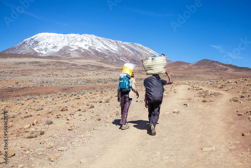 Porters carrying heavy load on his back walks along the road.