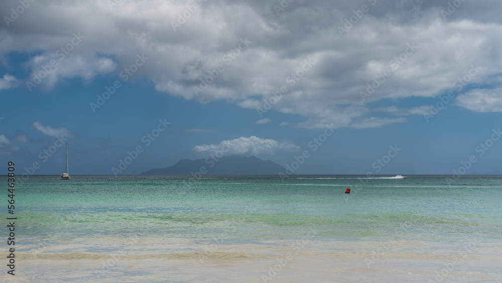 Sea idyll on a sunny day. A yacht is visible in the calm turquoise ocean. The outline of the island on the horizon. Clouds in the blue sky. Seychelles. Mahe. Beau Vallon