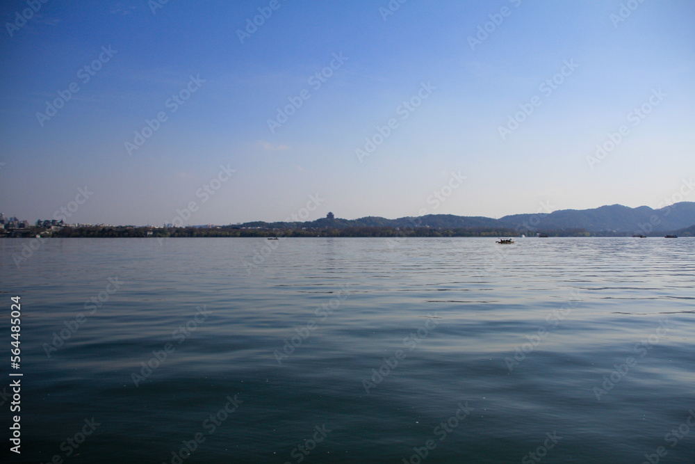 A silhouette boat sailing on the calm sea in the background of mountains and clear blue sky. For travel, background and blog etc. concepts. West Lake. Popular park of Hangzhou city China