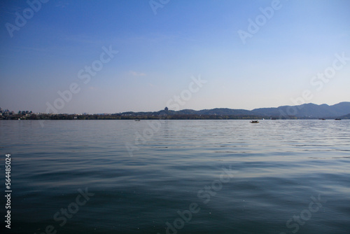 A silhouette boat sailing on the calm sea in the background of mountains and clear blue sky. For travel  background and blog etc. concepts. West Lake. Popular park of Hangzhou city China