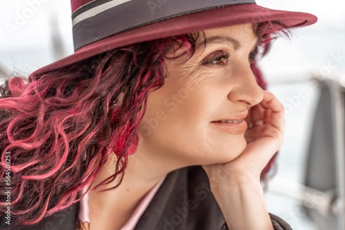 Portrait of a woman on a yacht in the sea, she has burgundy curly hair, looks to the side.