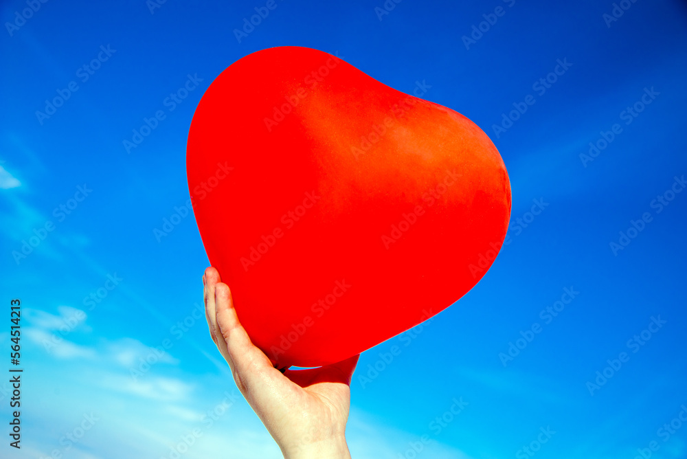 Fototapeta premium The girl holds the ball in the form of a heart against the blue sky 