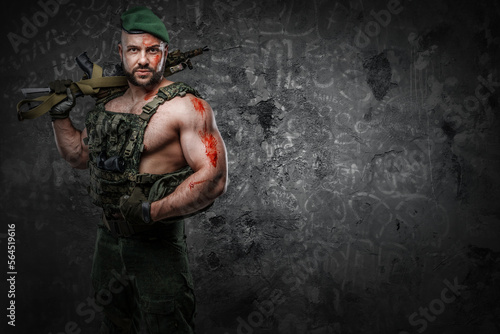Portrait of soldier with muscular build holding rifle dressed in vest.