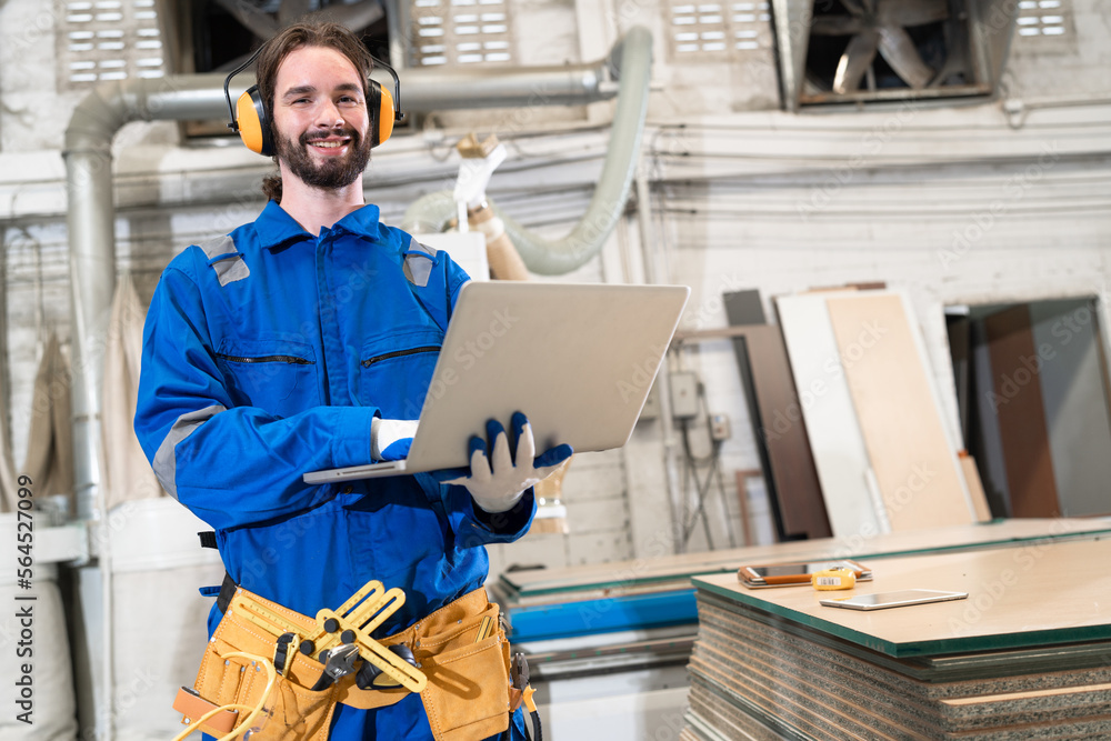 Handsome caucasian carpenter in safety blue uniform use notebook computer and checking machine at factory Handsome caucasian carpenter in safety blue uniform use notebook computer and checking machine at factory