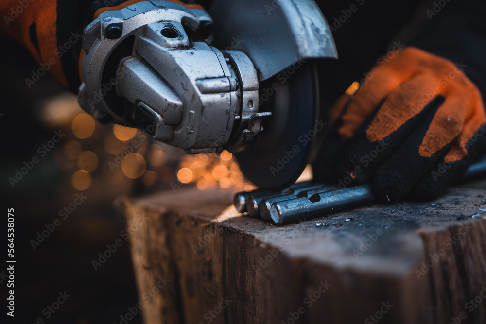 The hands of the master saw the metal with a grinder. Metal works in the workshop close up. Metal processing with angle grinder. Sparks in metalworking.