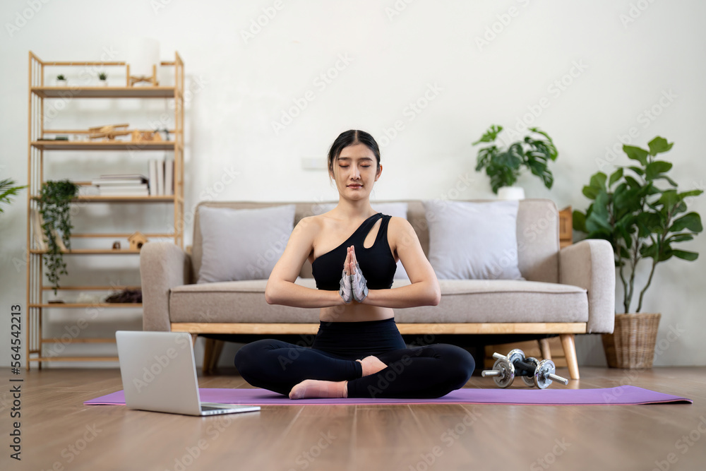 Millennial Asian woman meditating with trainer online on laptop at home Millennial Asian woman meditating with trainer online on laptop at home