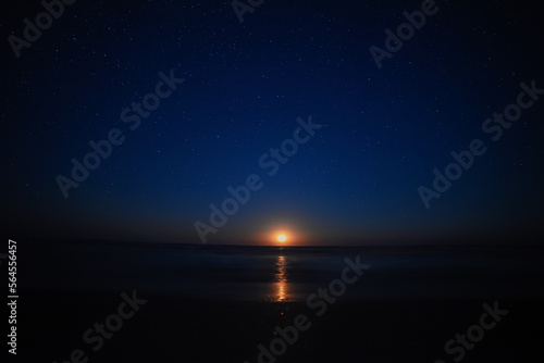 Moon rise by the sea with sky full of stars. Amazing orange moon is rising up. Nature astronomy night landscape.