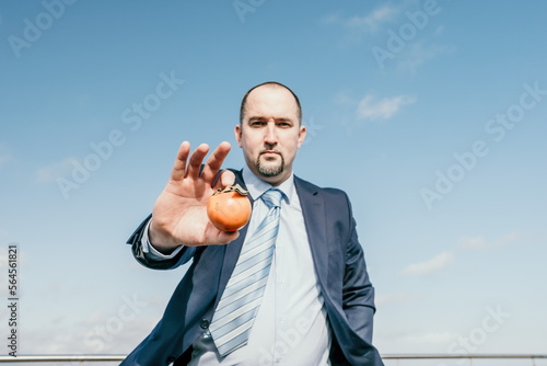Man persimmon park. Hipster millennial man in a tie and jacket bites off a persimmon while sitting on a park bench in slow motion Young business people eat golden persimmons at lunchtime.