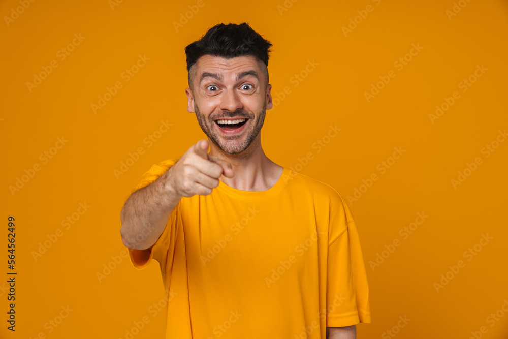 Smiling man pointing finger at camera isolated over yellow background Smiling man pointing finger at camera isolated over yellow background
