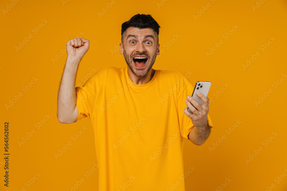 Excited guy making winner gesture while using mobile phone isolated Excited guy making winner gesture while using mobile phone isolated