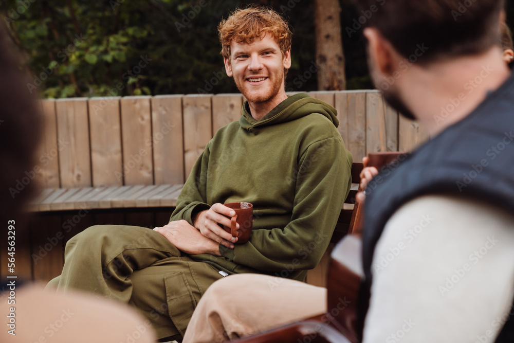 Cheerful guy drinking tea while spending time with friends in nature