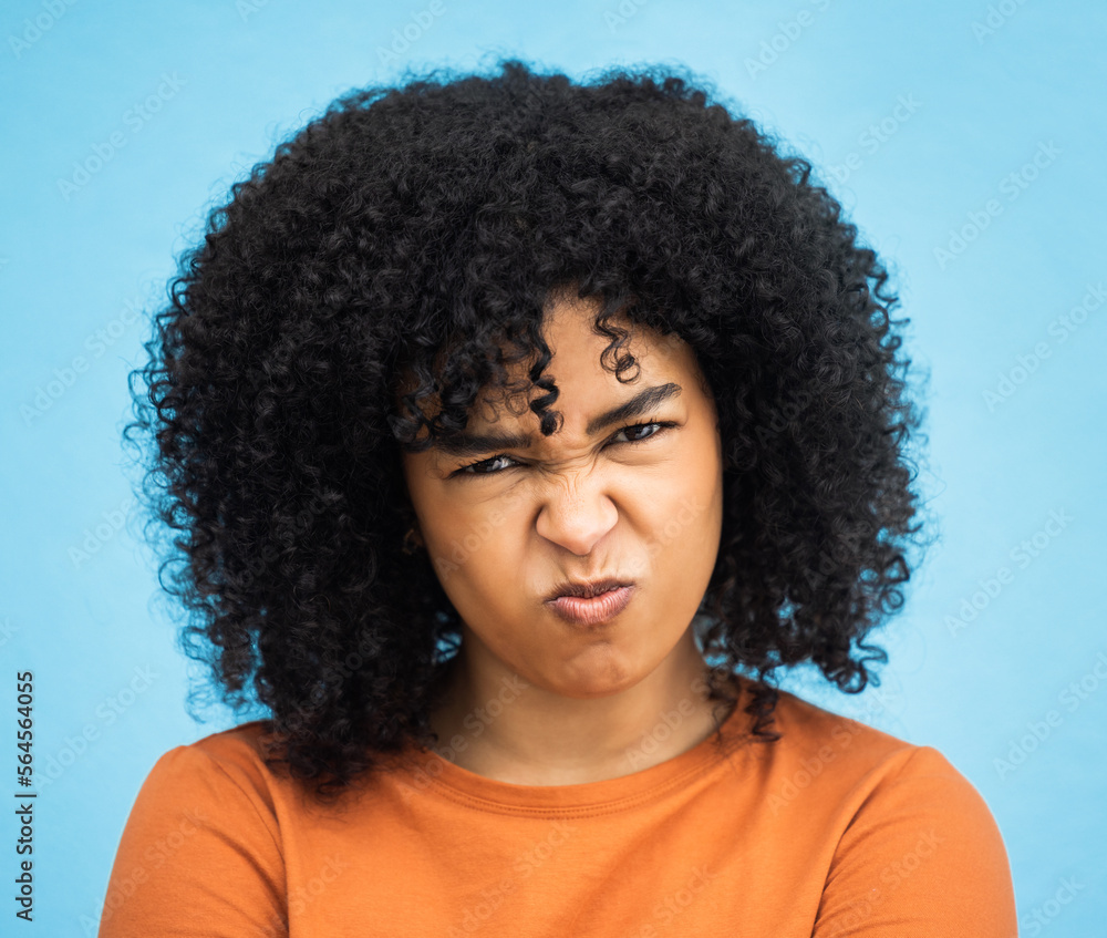 Black woman, portrait or angry facial expression on isolated blue background in mental health burnout. Headshot, model or person with mad, annoyed or frustrated face on backdrop mockup with afro hair Black woman, portrait or angry facial expression on isolated blue background in mental health burnout. Headshot, model or person with mad, annoyed or frustrated face on backdrop mockup with afro hair