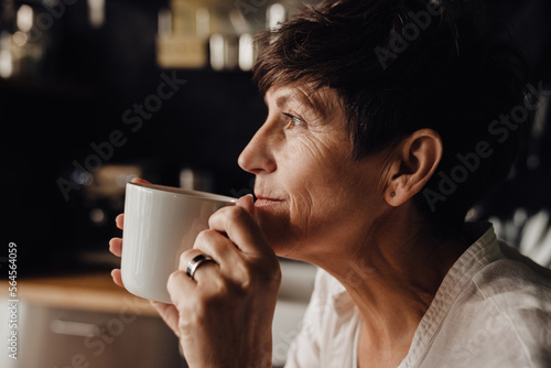 Smiling senior woman drinking coffee while sitting in kitchen