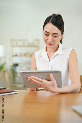 Gorgeous Asian woman using her tablet at the table in her minimal and cozy living room.