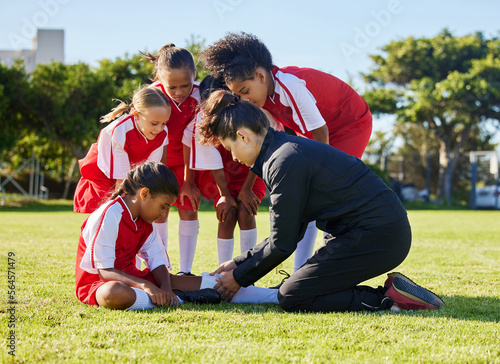 Accident, injury and children soccer team with their coach in a huddle helping a girl athlete. Sports, first aid and kid with a sore, pain or muscle sprain after a match on an outdoor football field.