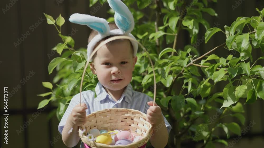 funny kid boy Easter bunny ears holding basket full of colorful easter eggs showing traditional Easter decorations on camera. Spring holiday celebration Easter. green fresh foliage tree, sunny day funny kid boy Easter bunny ears holding basket full of colorful easter eggs showing traditional Easter decorations on camera. Spring holiday celebration Easter. green fresh foliage tree, sunny day
