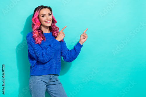 Photo of positive cheerful girl with curly hairdo dressed blue sweater directing empty space isolated on vibrant teal color background