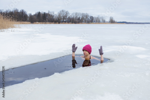 Winter swimming. Woman in frozen lake ice hole. Swimmers wellness and endorphin booster swim in cold water. Beautiful female body tempering Cold winter morning landscape. Biohacking routine