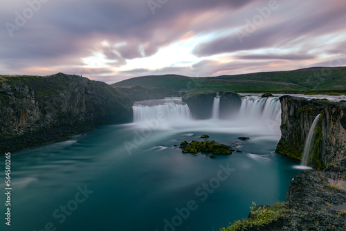 Long exposure sunset landscape over the icelandic Godafoss waterfall with blurred water falling into turquoise river and cloudy majestic sky