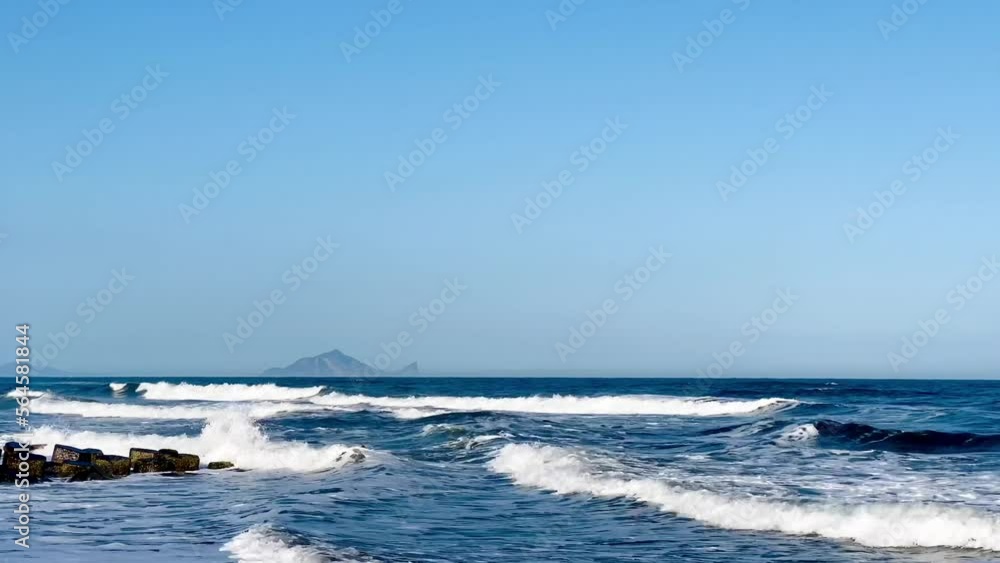 Blue ocean waves. Waves splash on the sea sand. There is a turtle-shaped island, Guishan Island (Turtle Island) in the distant sea. Blue ocean waves. Waves splash on the sea sand. There is a turtle-shaped island, Guishan Island (Turtle Island) in the distant sea.