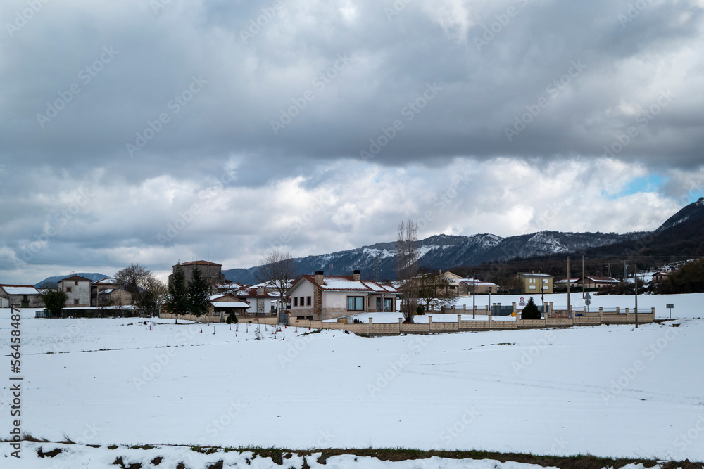 Pequena aldeia com montanhas ao fundo com um manto de neve num dia frio de inverno em Espanha