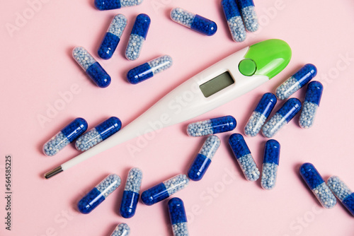 Electronic thermometer and blue pills on pink paper background with copy space, flatlay