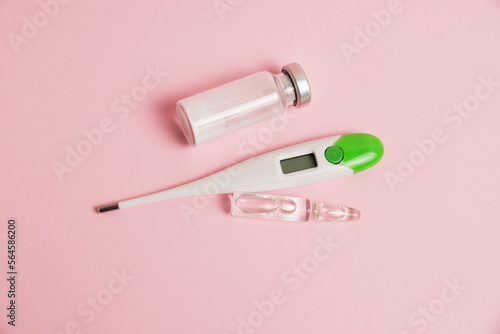Electronic thermometer and ampoules on pink paper background with copy space, flatlay