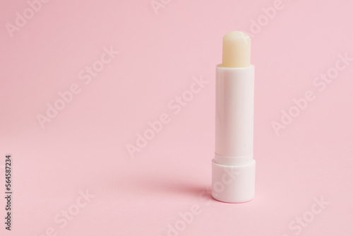 Transparent sanitary lipstick on pink paper background with copy space