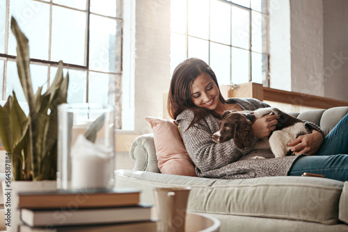 Woman relax on couch with puppy, happy and content at home with pet, happiness together with peace in living room. .Female cuddle dog, love for animals with smile and care, stress relief and comfort