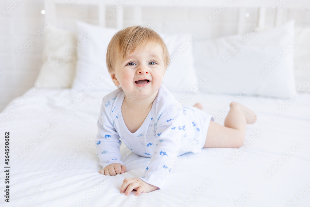 a capricious baby boy of six months blonde wants to sleep or cries on the crib lying on his stomach in a room at home with white cotton bedding, the concept of children's goods and accessories a capricious baby boy of six months blonde wants to sleep or cries on the crib lying on his stomach in a room at home with white cotton bedding, the concept of children's goods and accessories