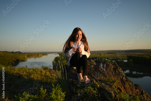 A teenage girl walks through the mountains  across the field. A happy young girl with long hair  standing in the wind. A walk in the fresh air.