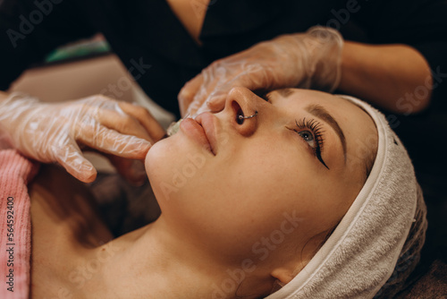 Close up of hands of cosmetologist making botox injection in female lips. She is holding syringe. The young beautiful woman is receiving procedure with enjoyment