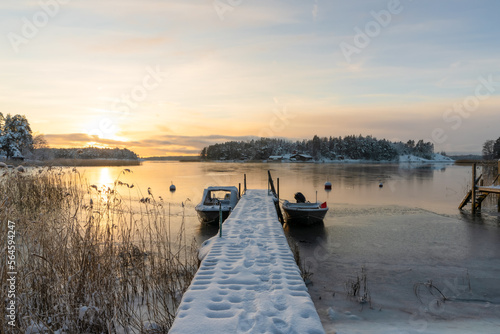 Soukka, Finland - 09.12.22: Winter sunset over the snow-covered islands in the bay. Frozen bay. Pier with boats in the foreground. Winter landscape. Scandinavia.