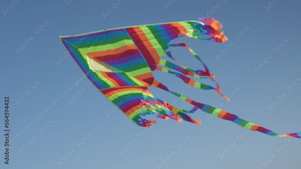 colorful kite fly in blue sky, striped rainbow kite flying in air. happy summer holidays concept: toy kite moves in blue sky with long rainbow color tail. sunny weather warm daytime colorful kite fly in blue sky, striped rainbow kite flying in air. happy summer holidays concept: toy kite moves in blue sky with long rainbow color tail. sunny weather warm daytime