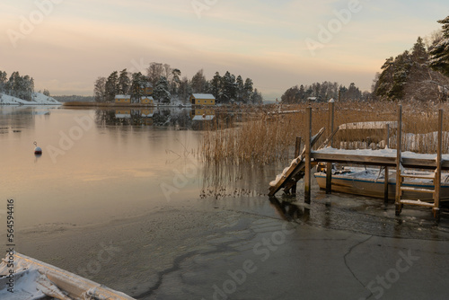 Soukka, Finland - 09.12.22: View from the shore of a small snow-covered island with houses. Frozen bay. Wooden pier in the foreground. Winter landscape. Scandinavia.