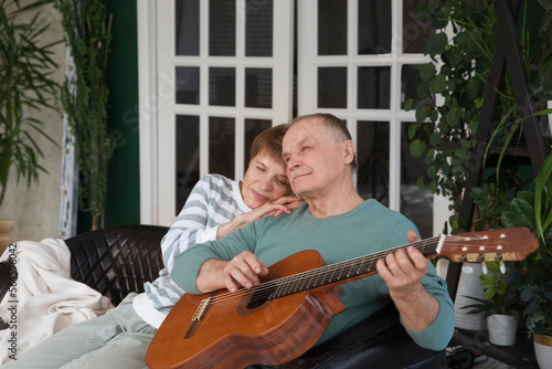 elderly couple spend time together. healthy lifestyle. emotional health. rest from gadgets. an elderly man plays guitar for his wife sitting on the couch at home. Happy Valentine's Day