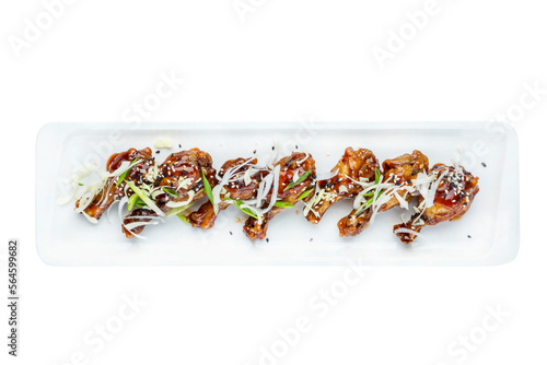 Appetizing chicken legs marinated with green onions on a white snack plate. Close-up. Top view. Isolated on white background.