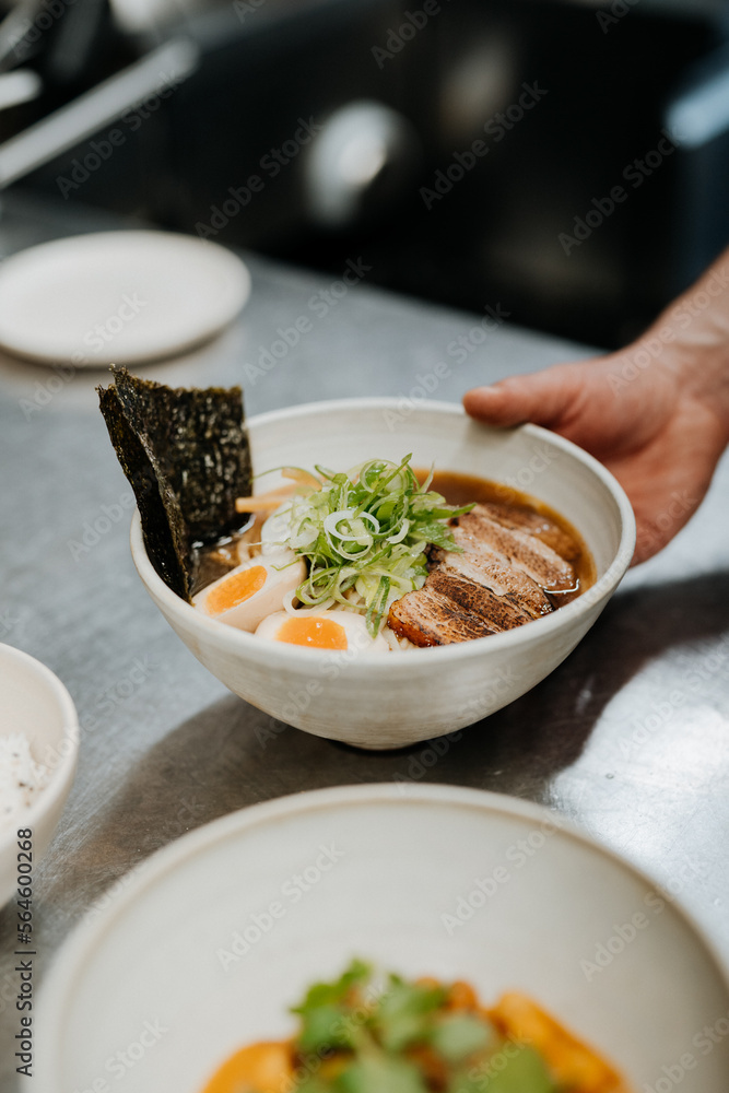 Hand of unrecognizable waiter serving asian noodle soup, ramen in white bowl Hand of unrecognizable waiter serving asian noodle soup, ramen in white bowl