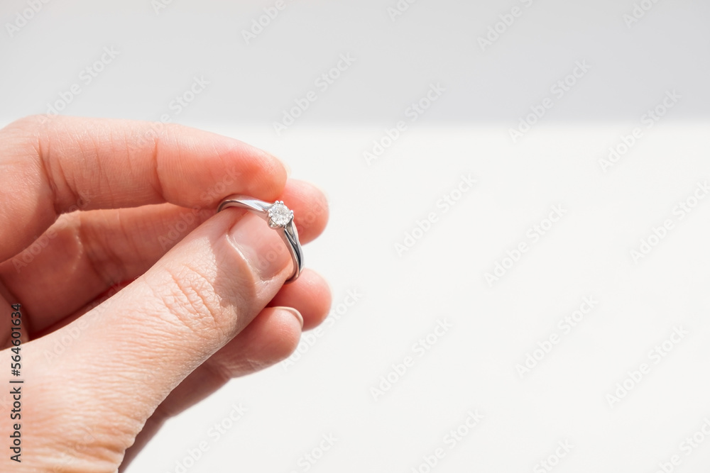 Close up of woman hand holding elegant diamond ring on white background. Diamond engagement brilliant ring.