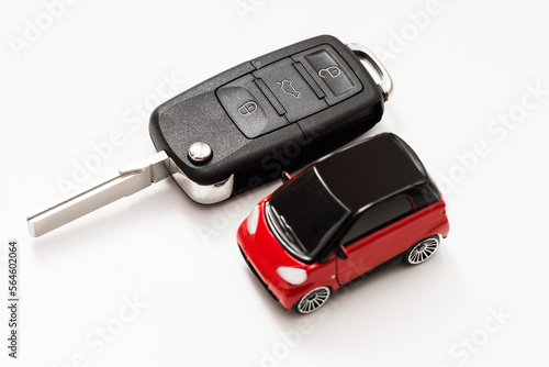 Red car with black roof next to a black car key on white background. Focus on the car.