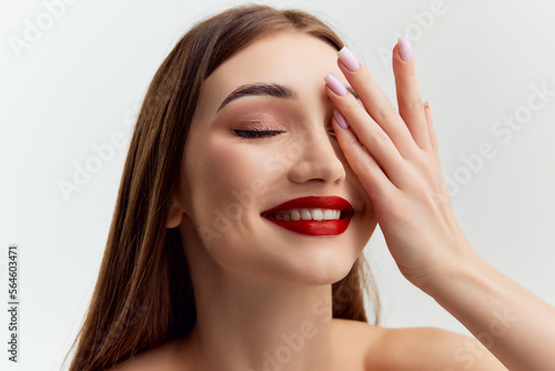 Young beautiful brunette girl with red lips makeup posing over grey studio background. Looking shy. Smiling. Concept of natural beauty  youth  fashion  cosmetology  wellness  makeup.