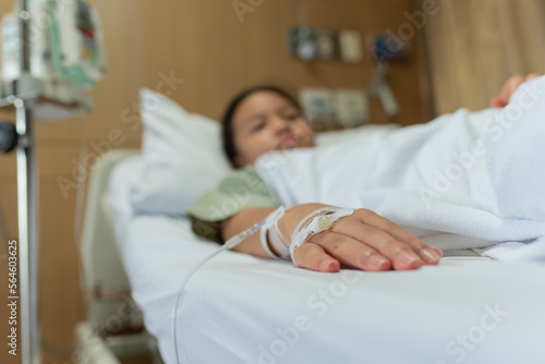 Young patient asian woman lying on bed in hospital with IV saline drip to back of the hand, teenager sick in hospital, Selective focus, healthcare and health insurance concept.