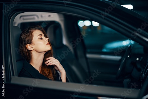 a stylish, luxurious woman is sitting in a black car at night, straightening her long, styled hair, closing her eyes with pleasure