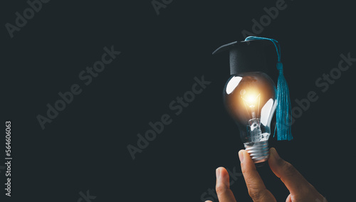 academy and success graduate education concept. businessman hand holding bright, electric light bulb with degree cap on black background. business education, knowledge, learning idea with copy space. photo