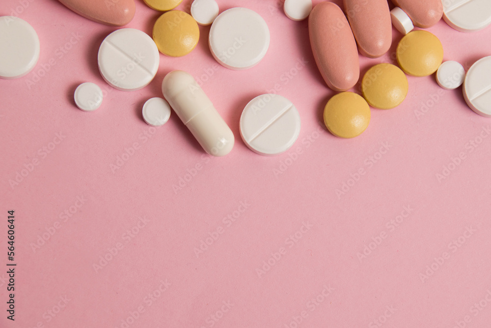 Flatlay, many different pills on pink background with space for text below